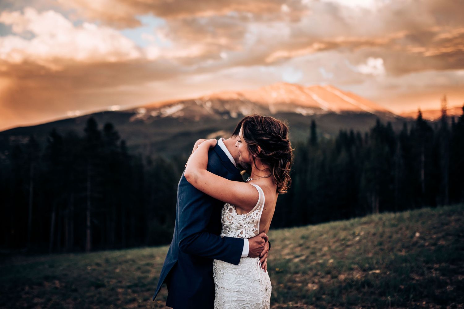 Intimate wedding photograph with mountain backdrop and dramatic orange sky.