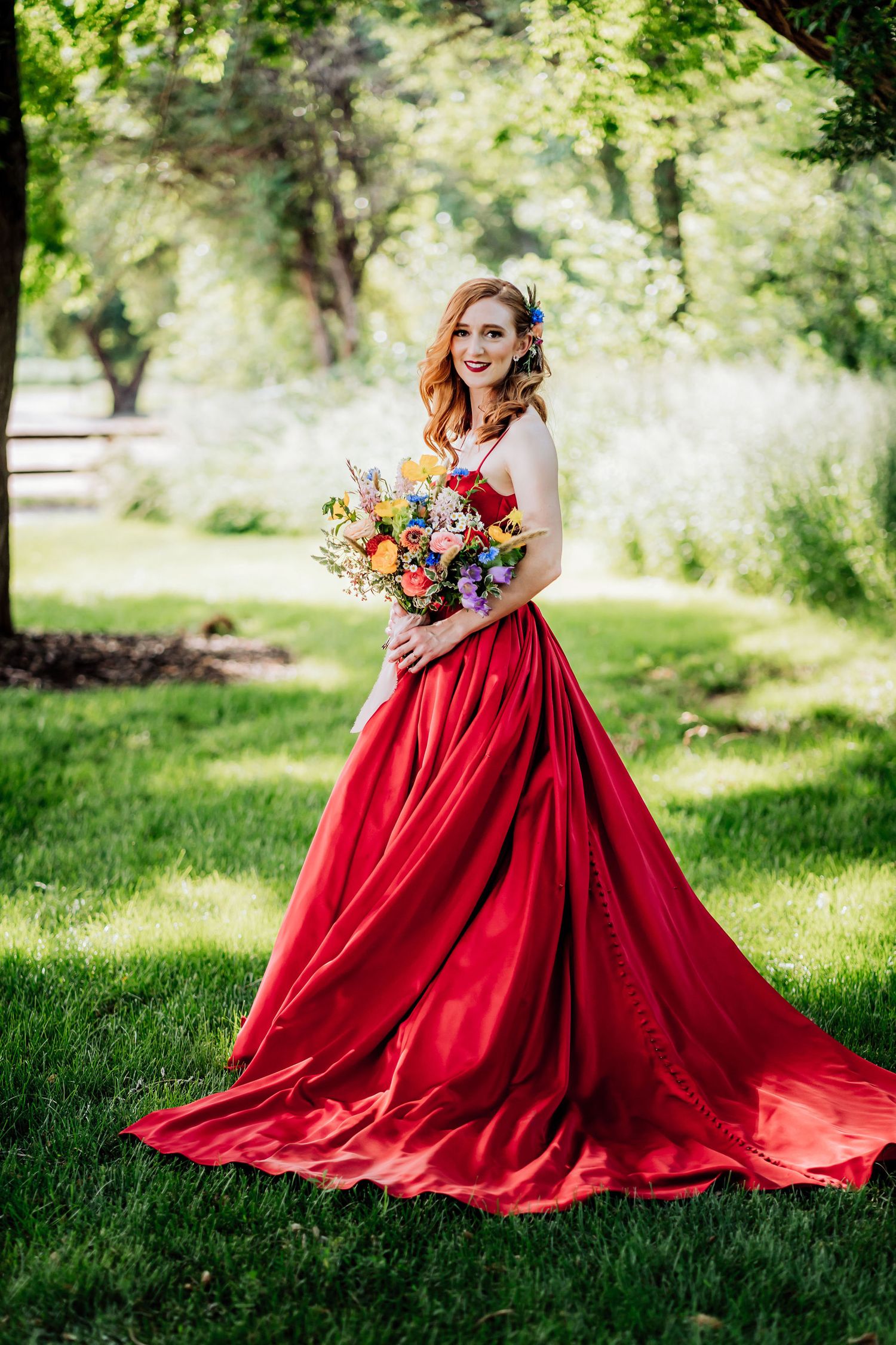 Stunning red ballgown and colorful bouquet photographed in sunlit garden setting.