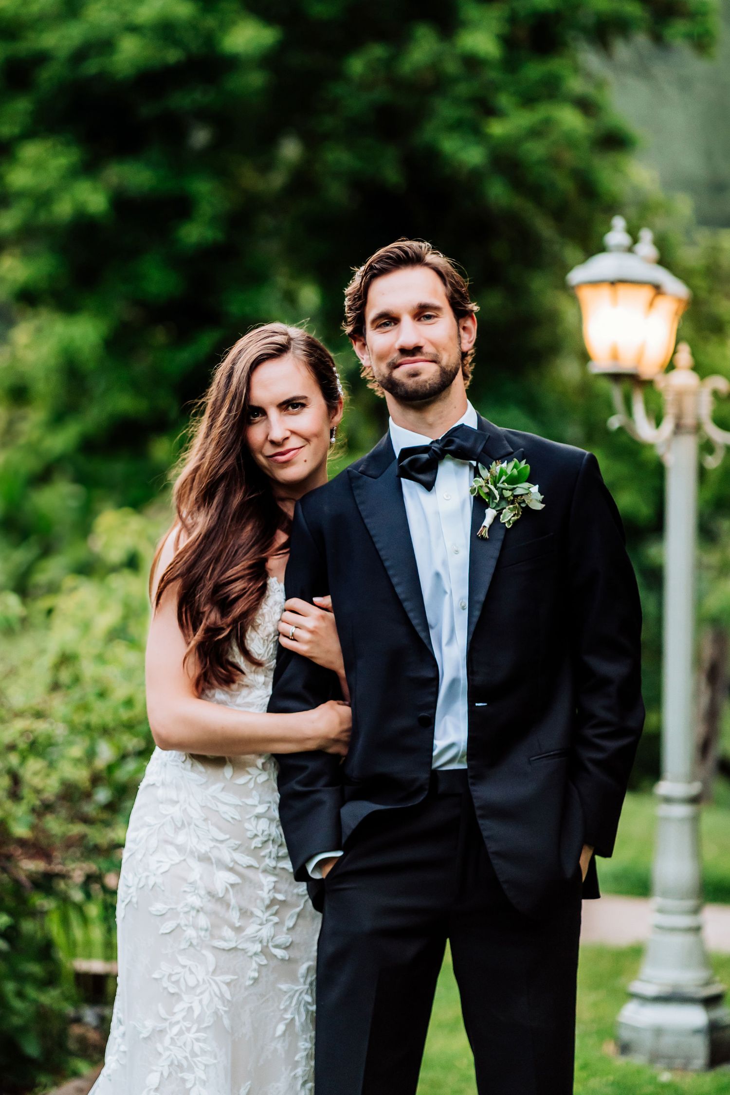 A couple poses for formal wedding portraits in an elegant garden setting at dusk.
