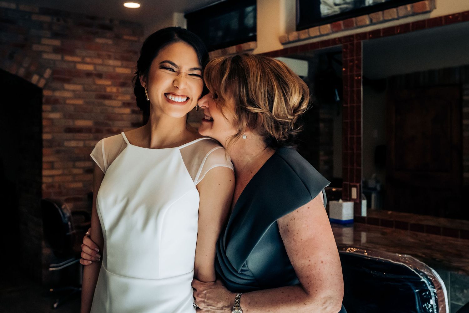 Tender moment shared during wedding preparations in front of exposed brick wall.