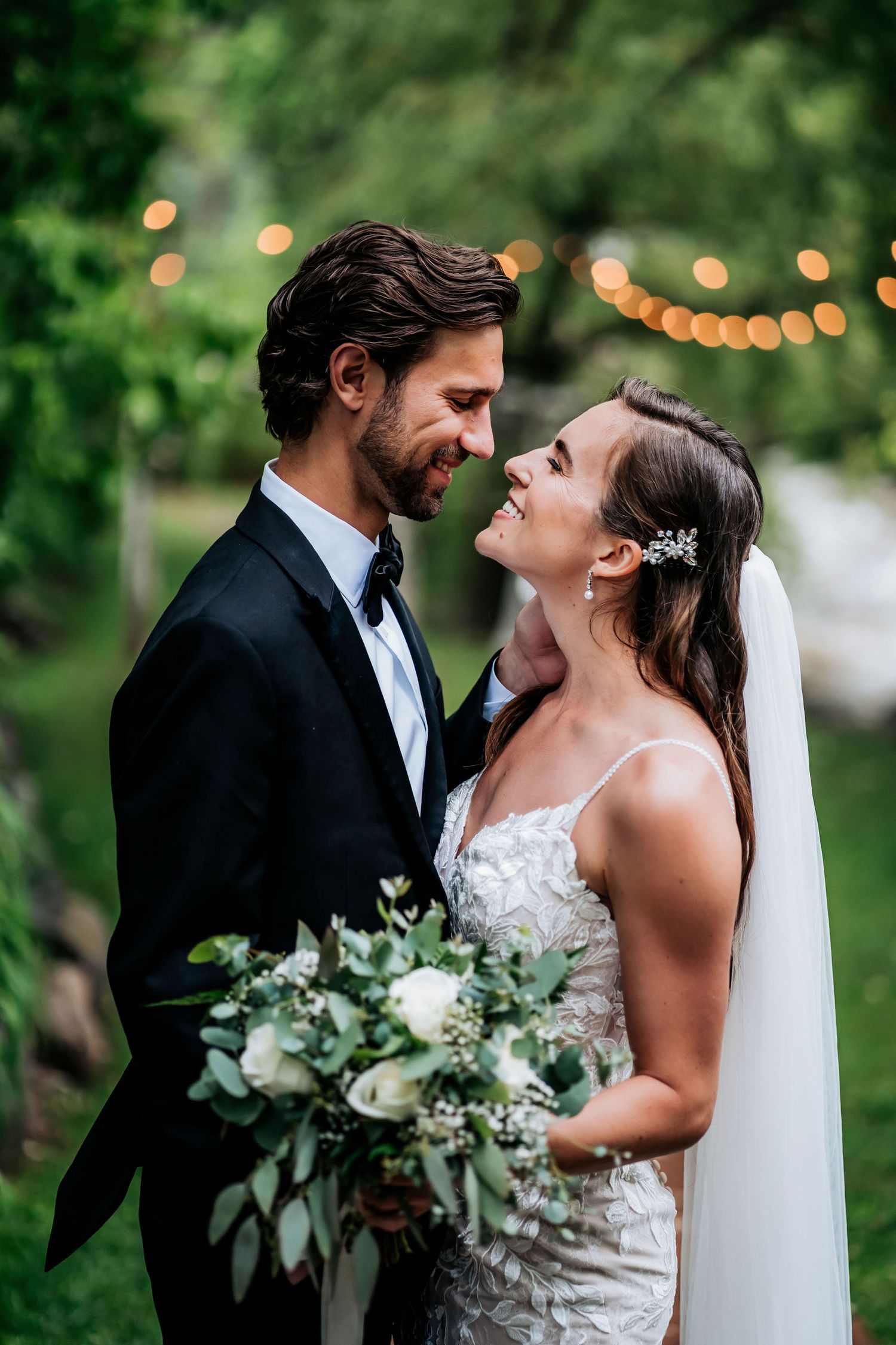 Romantic wedding portrait with string lights and greenery in the background.