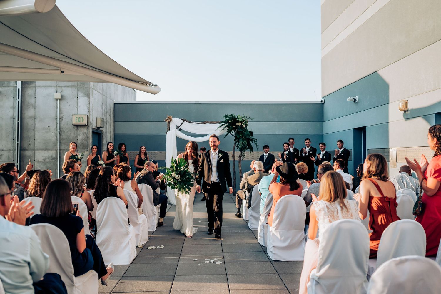 Rooftop wedding ceremony with white chairs and draped fabric arch against urban backdrop.