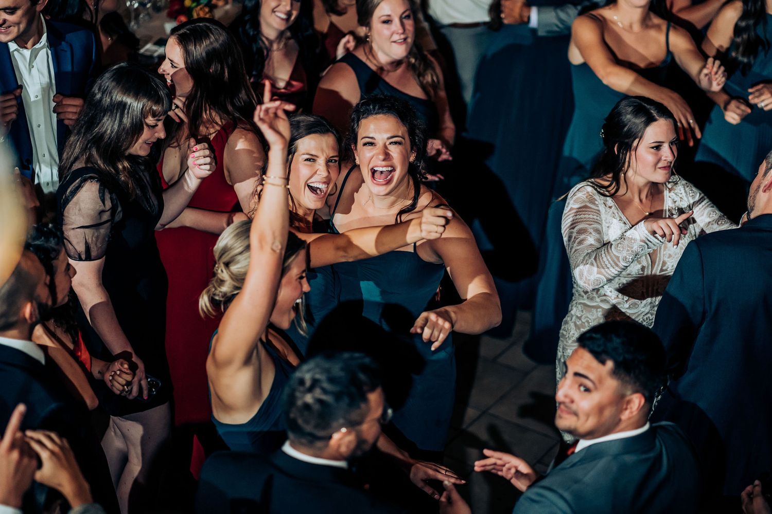 Wedding guests dance and celebrate on a crowded reception dance floor.
