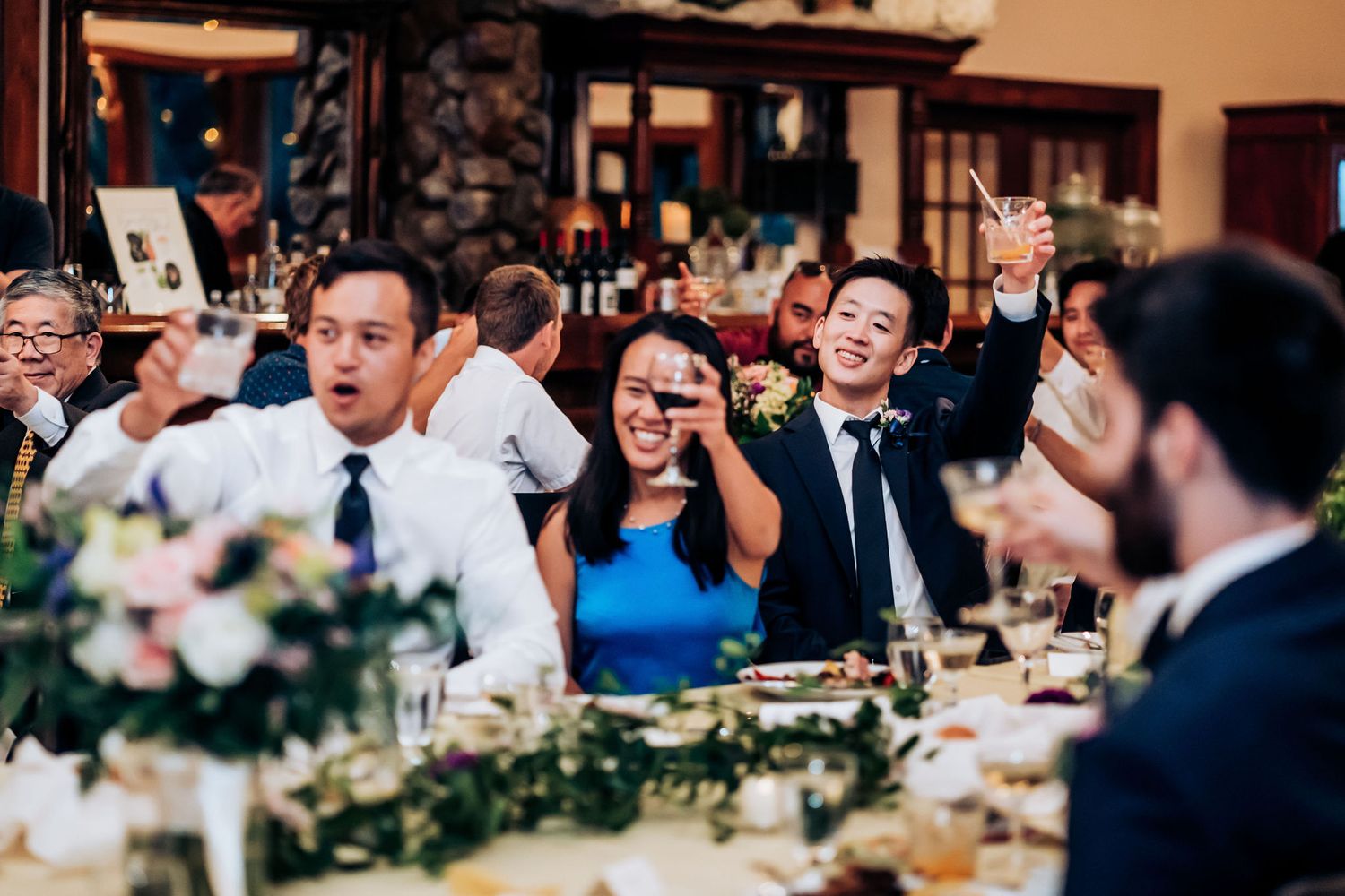 Energetic wedding reception scene with guests cheering and celebrating at decorated dinner tables.