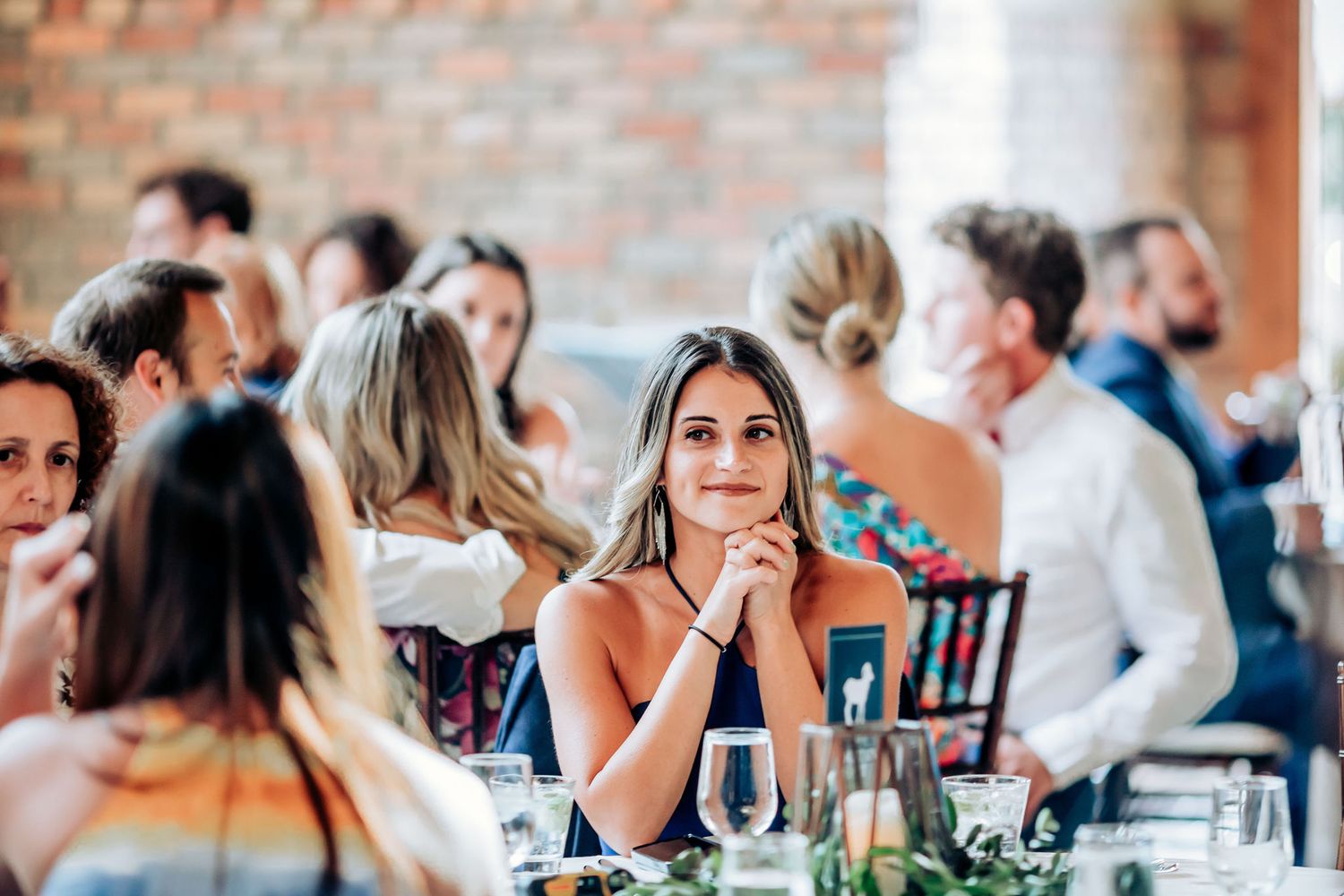 Wedding guests enjoying the reception dinner at decorated tables in a brick-walled venue.