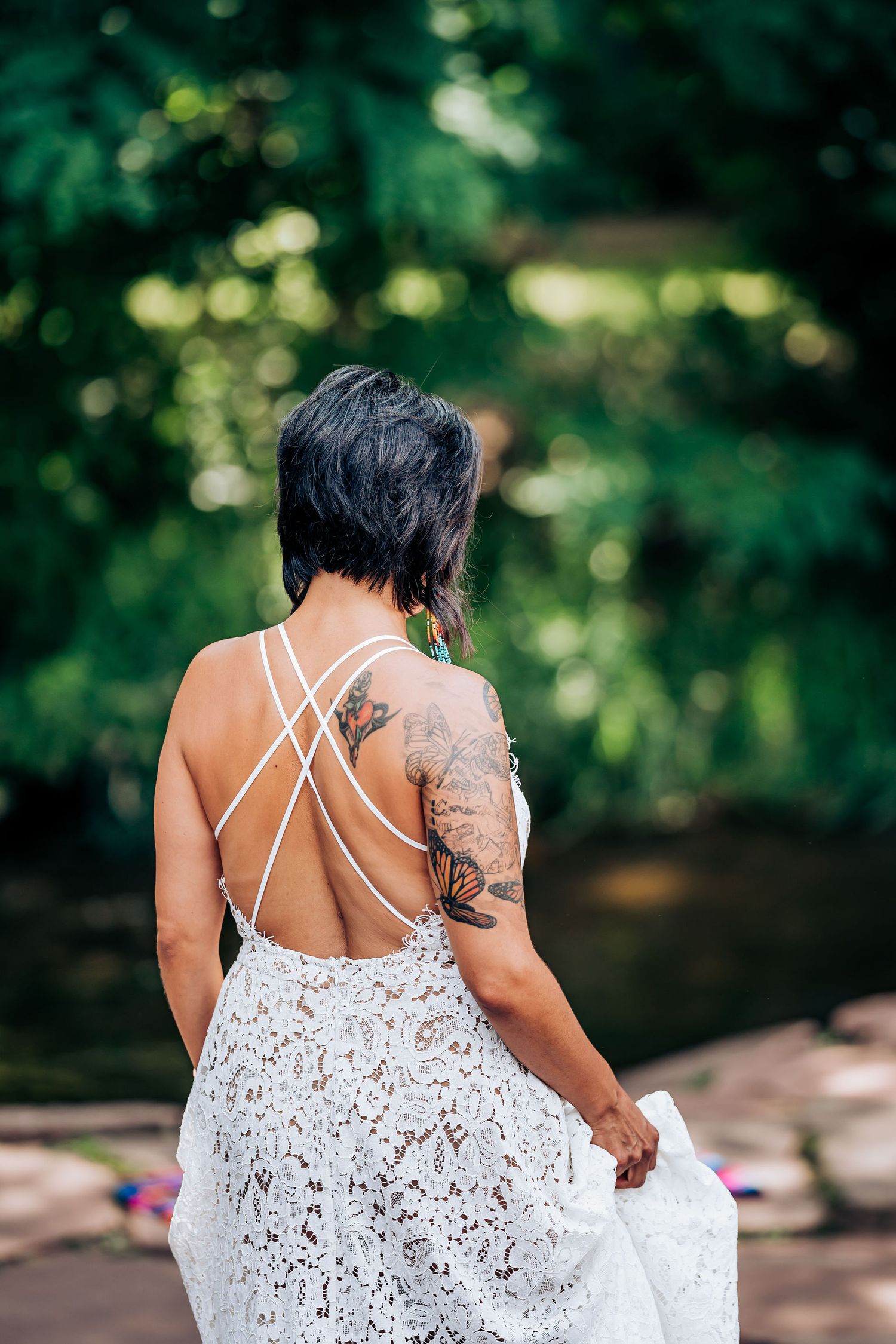 Back view of lace wedding dress with strappy details and visible tattoo in garden setting.