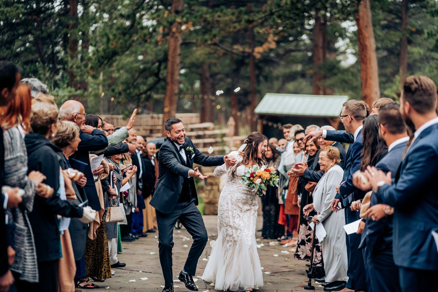 Wedding guests celebrate along pathway as couple makes joyous exit through crowd.