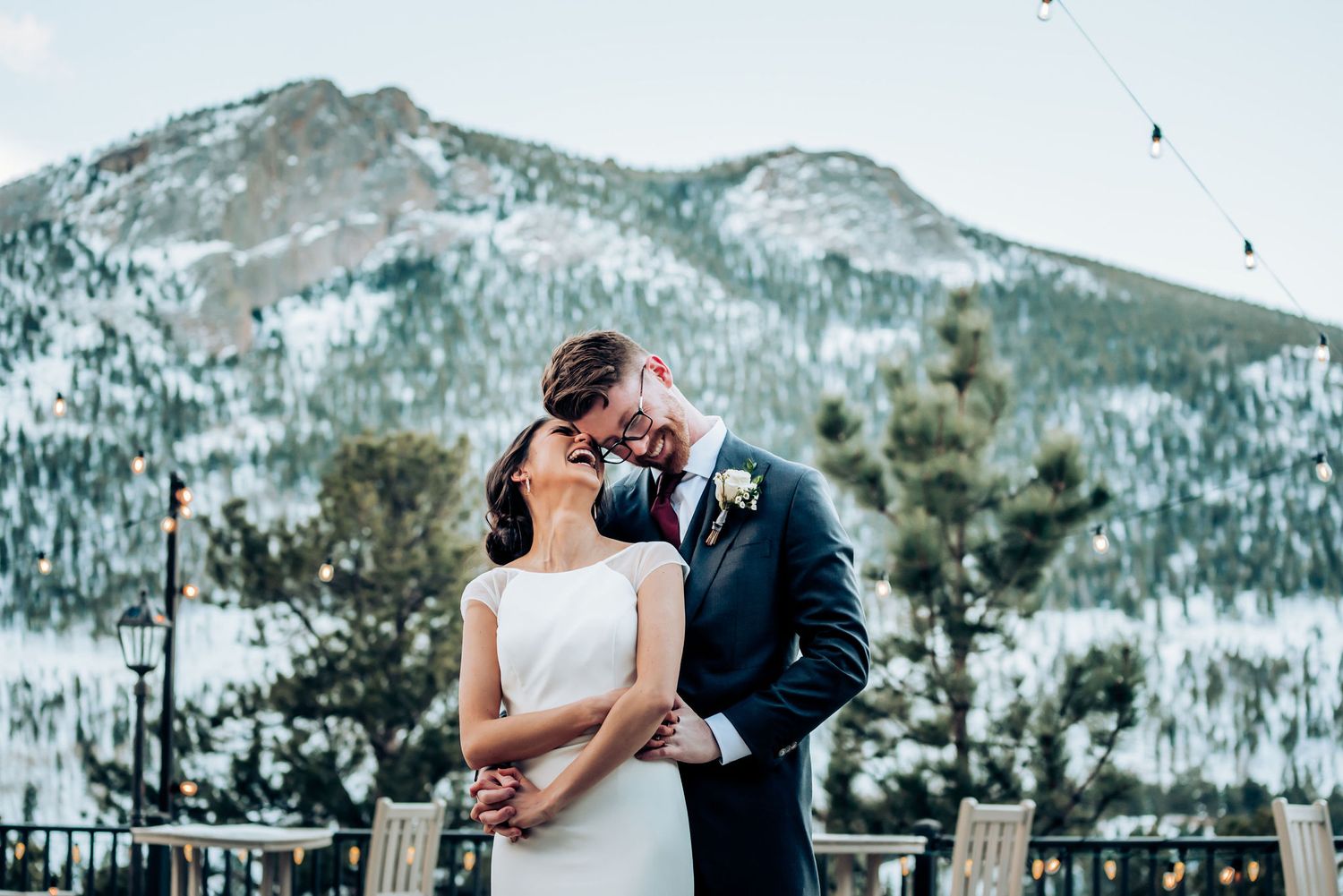 Intimate moment between newlyweds on a mountain terrace with snow-covered peaks in background.