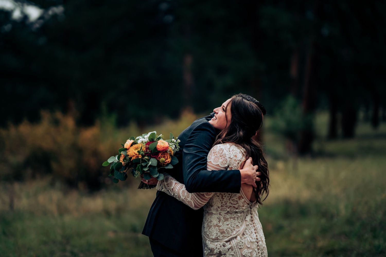 Tender embrace between newlyweds with vibrant autumn bouquet in forest setting.