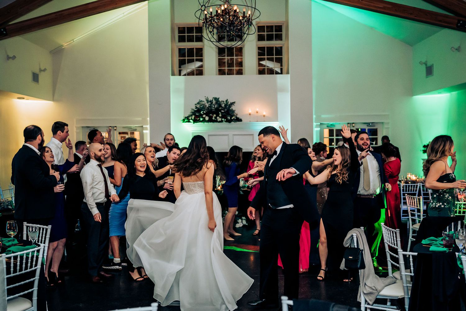 Wedding celebration with guests dancing in a reception hall illuminated by colorful lighting.