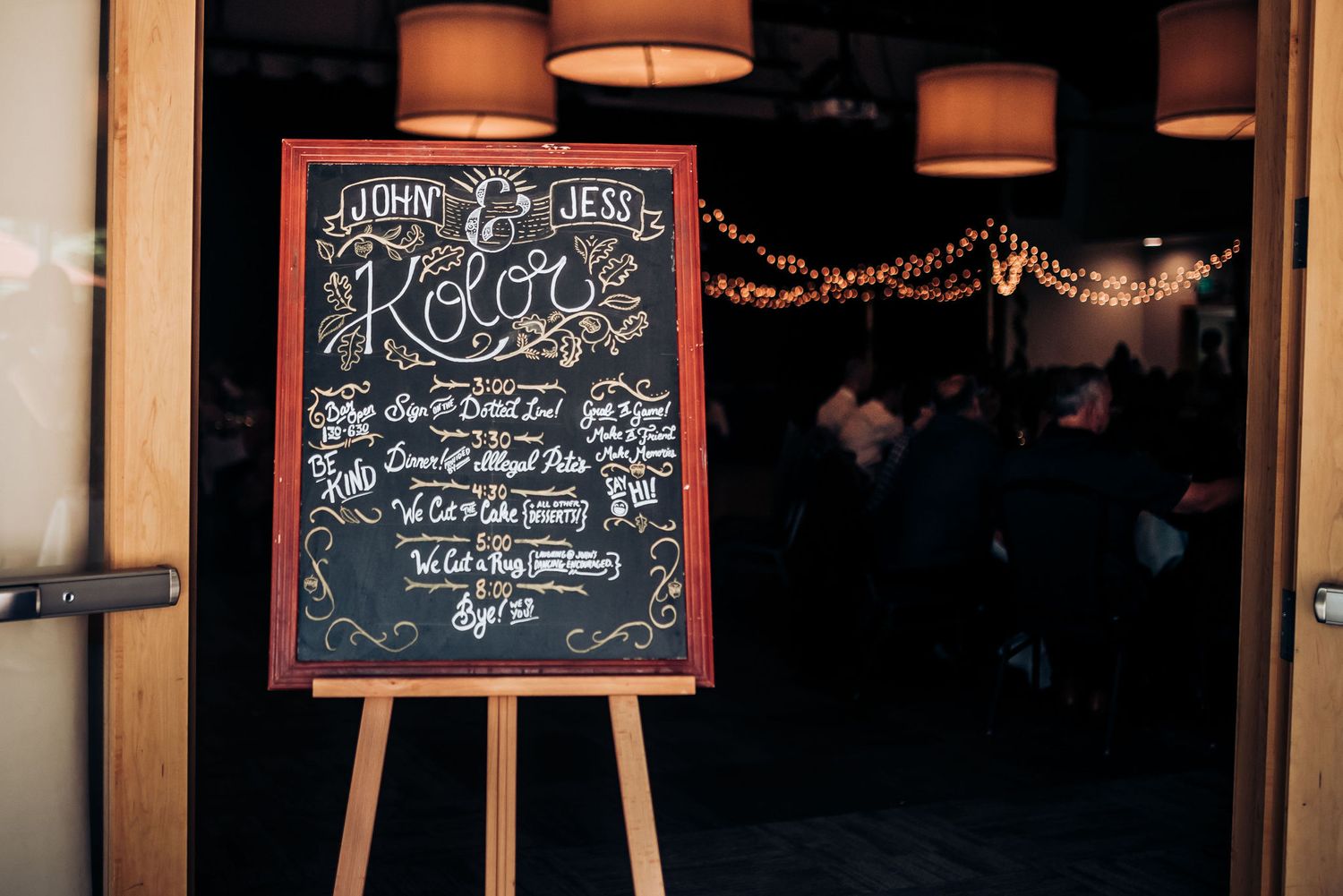 Rustic chalkboard menu sign displayed on wooden easel with string lights in background.