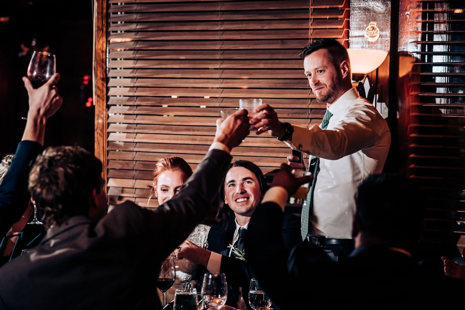 Celebratory moment during wedding speeches with guests raising glasses in a restaurant setting.