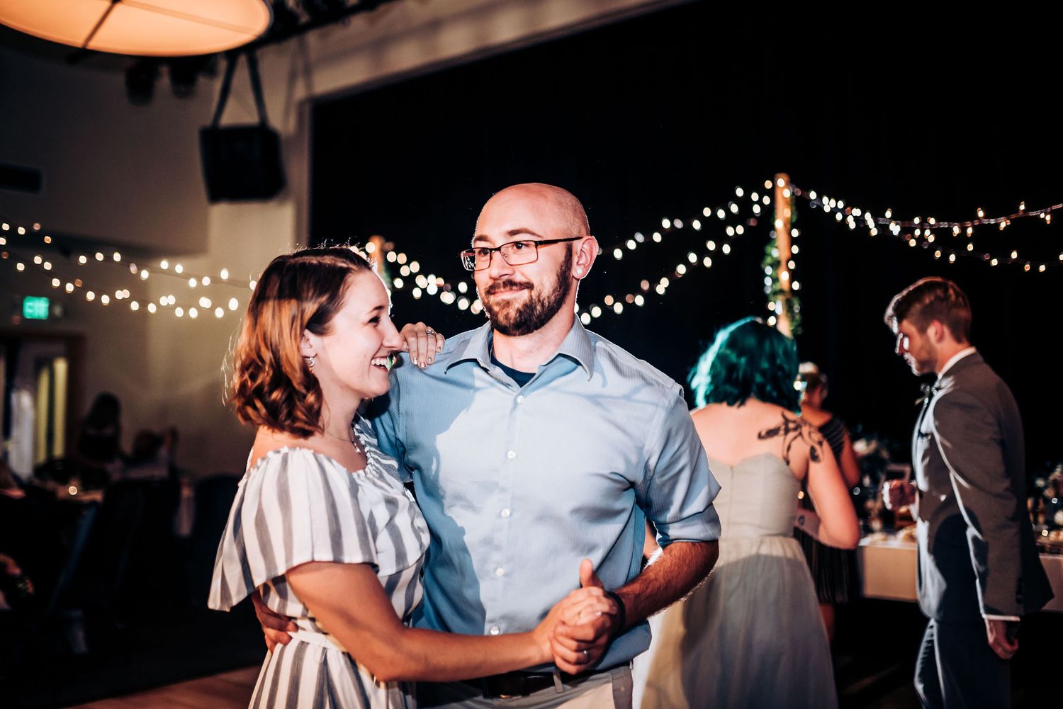 Couples dancing together at evening reception under decorative string lights.