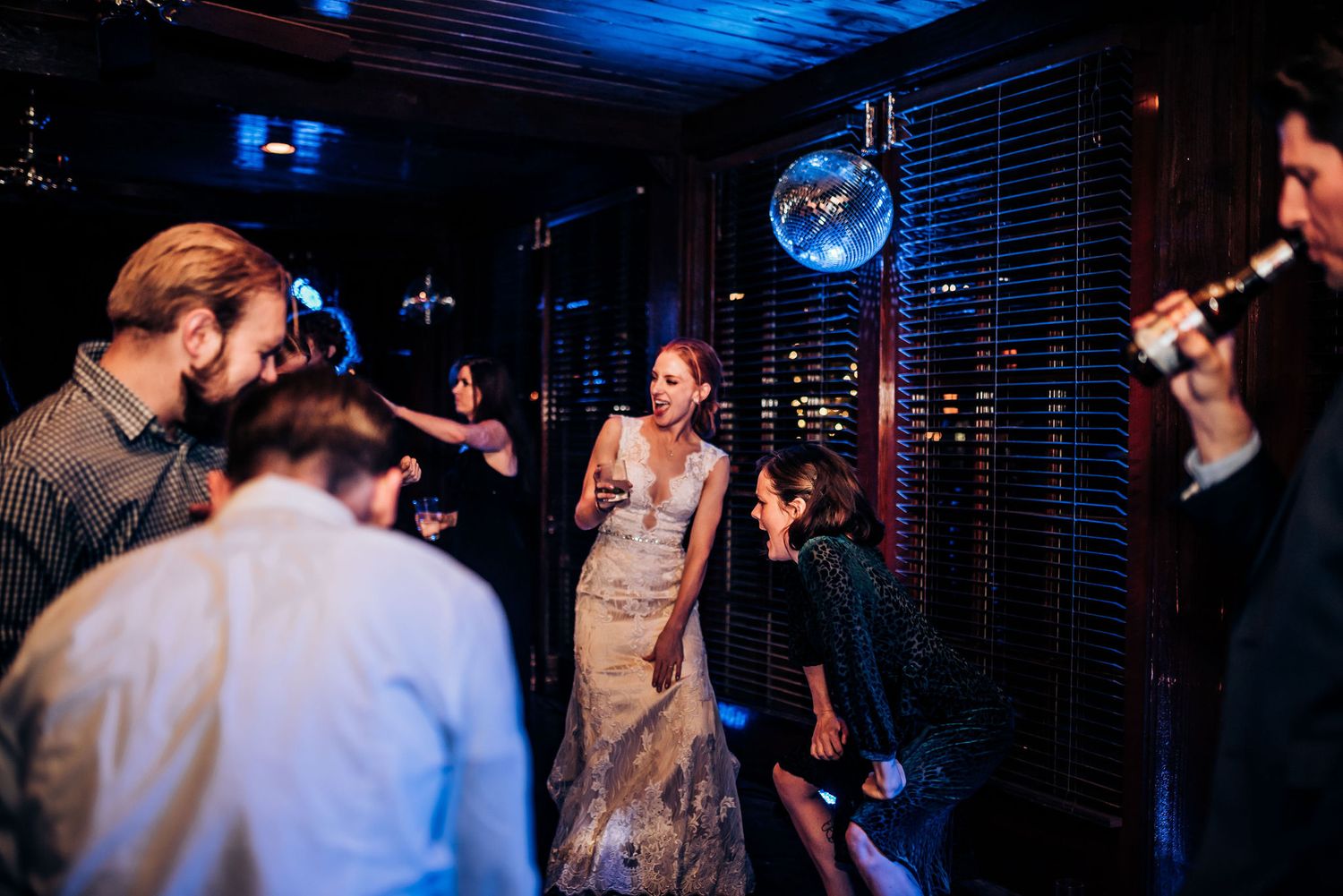 Wedding reception guests dance and celebrate in a dimly lit venue.