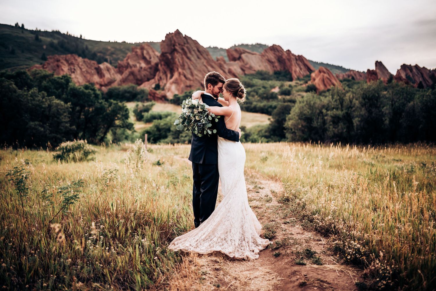Wedding couple shares intimate moment on trail with red rock formations in background.