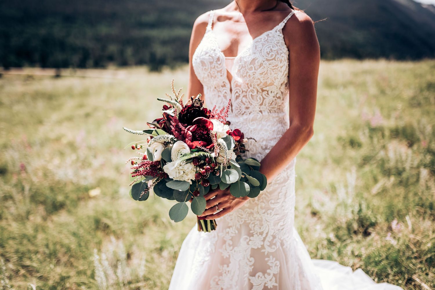 A detailed shot of burgundy and white wedding bouquet with eucalyptus against a lace dress.