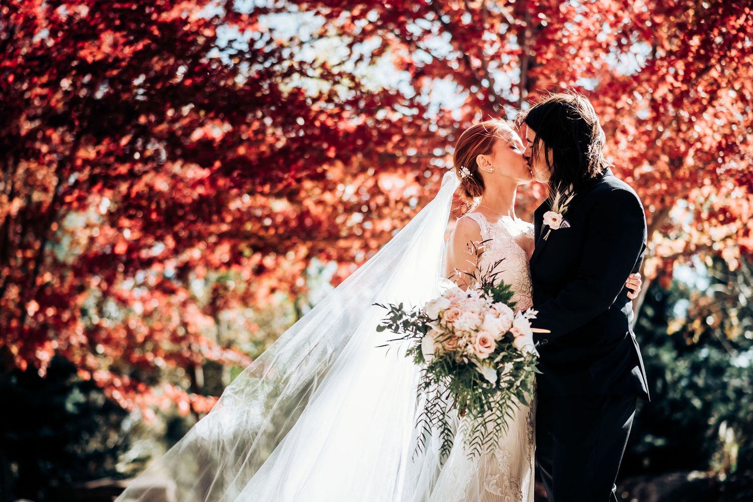 Wedding couple embraces under spectacular red fall foliage during their outdoor ceremony.