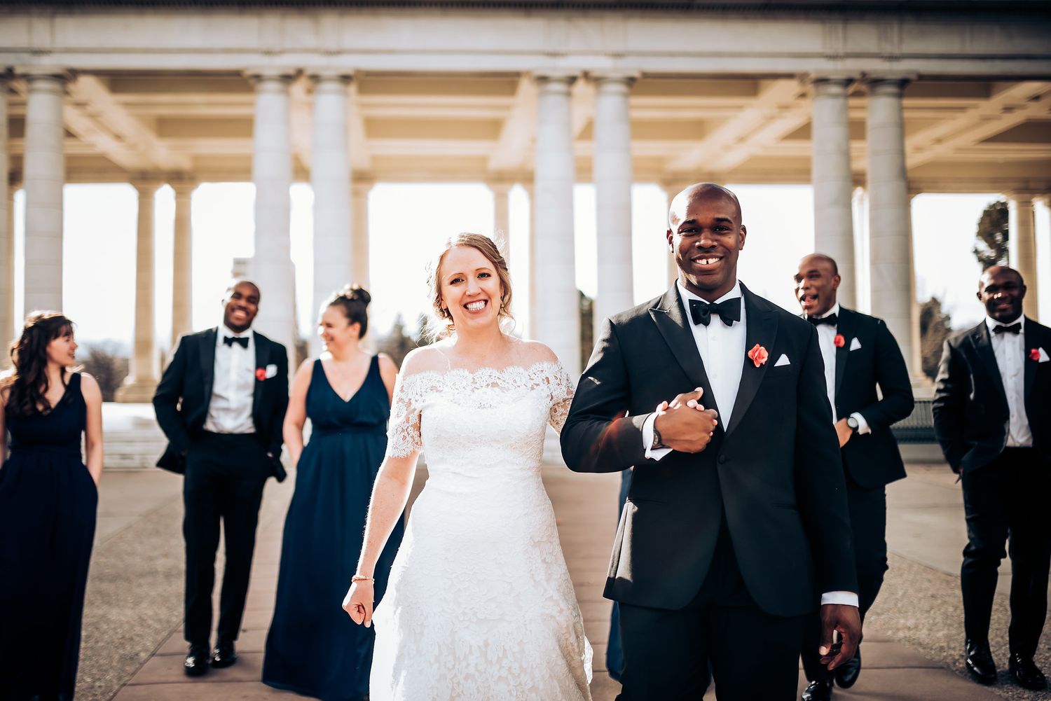 Wedding party poses outdoors with bridesmaids in navy and groomsmen in black tuxedos.