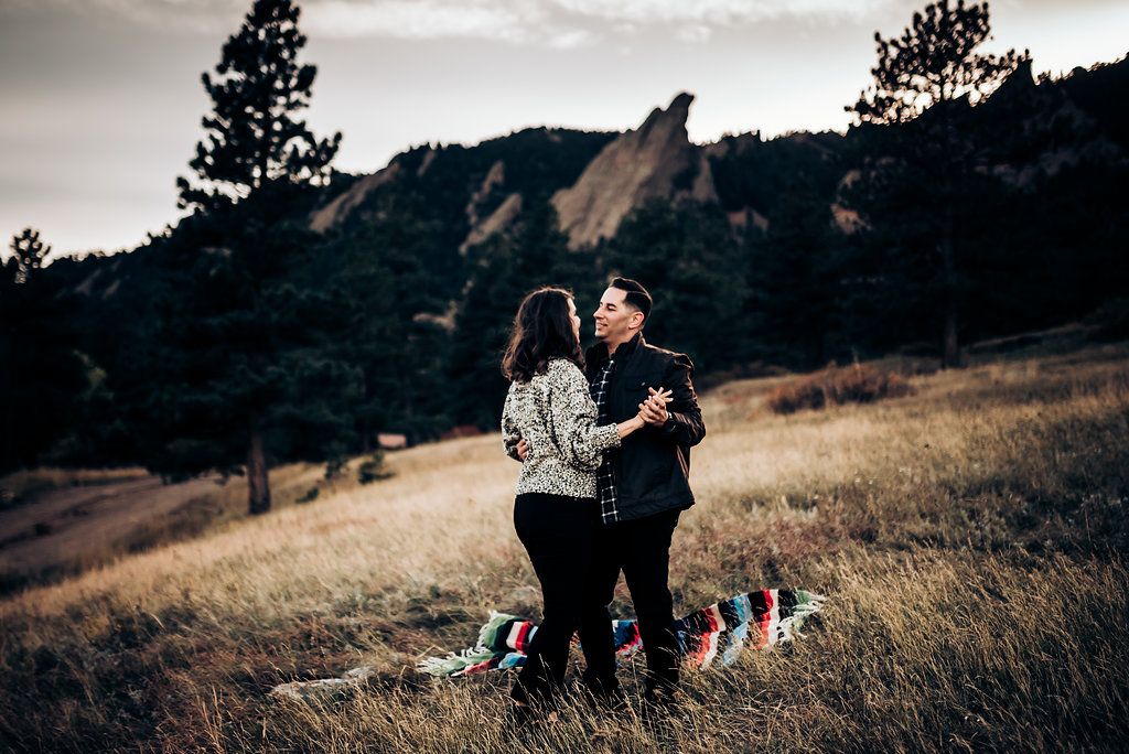 Couple embracing on a hillside with dramatic rocky mountain formations in the distance.