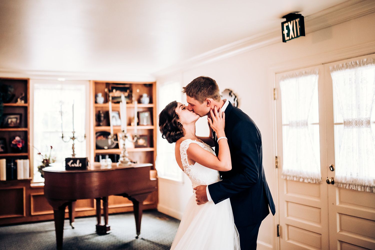 A romantic kiss between newlyweds in a room with classic furniture and built-in bookshelves.