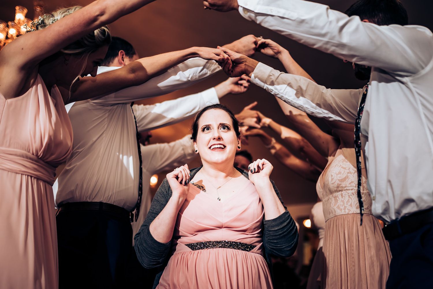 People making a tunnel with their arms at a reception while someone dances underneath.