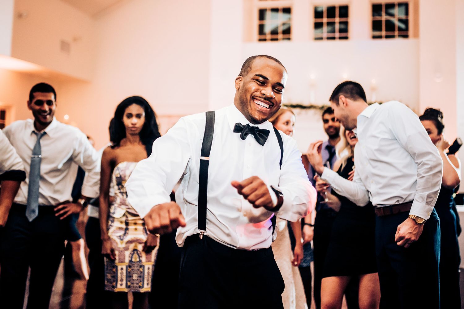 Reception guest dances enthusiastically in suspenders and bow tie.