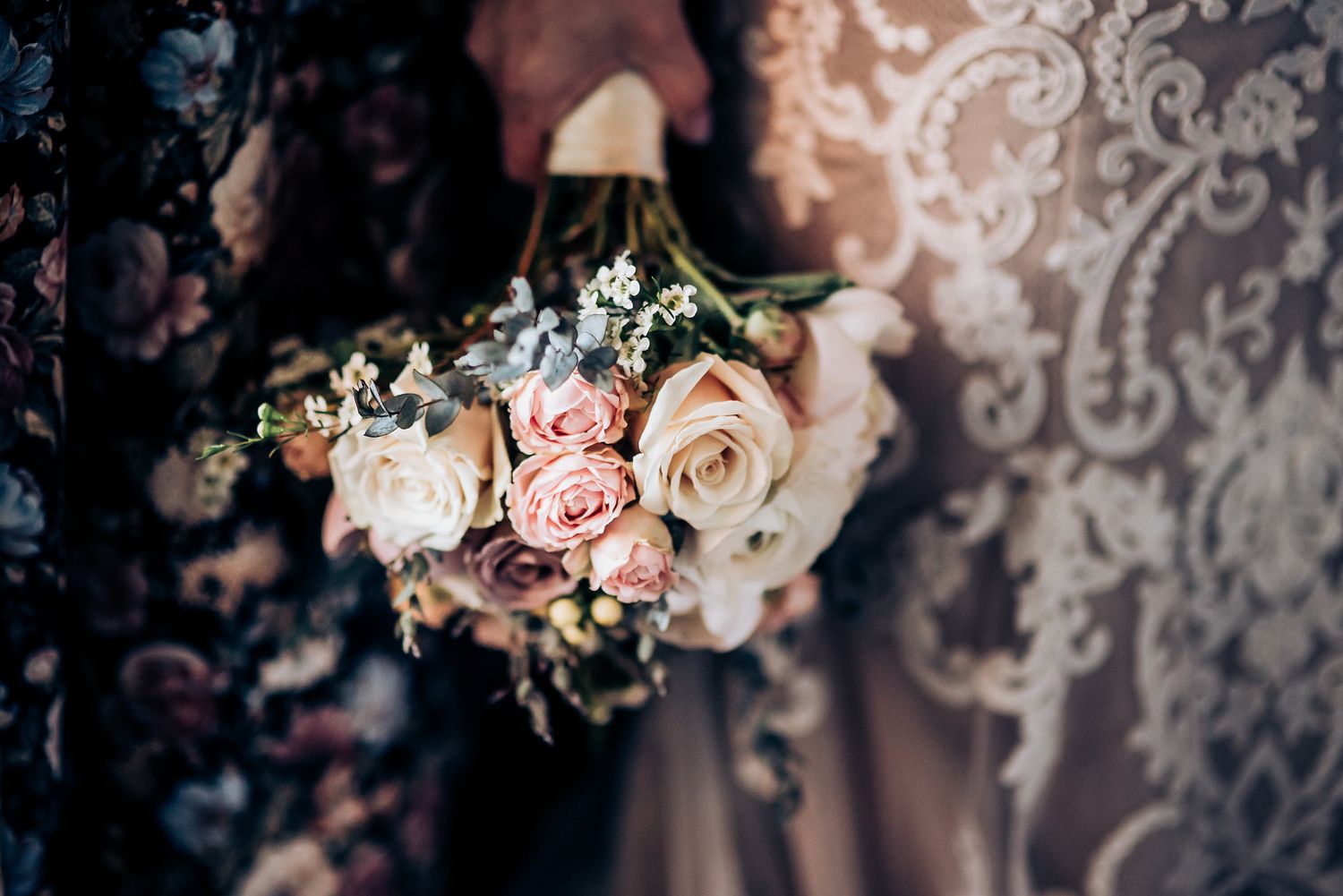 Close-up of blush and cream rose wedding bouquet against floral wallpaper.