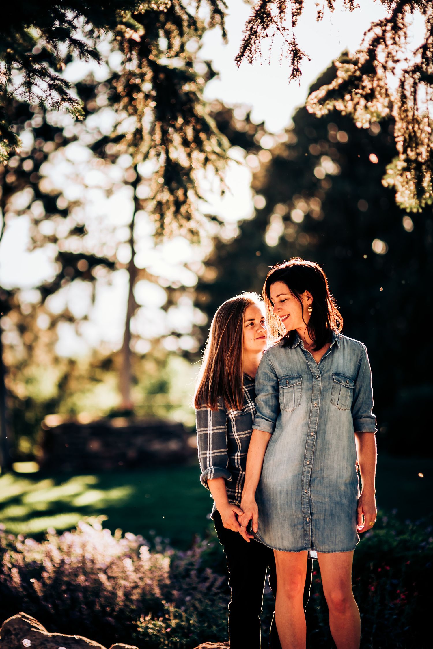 Two people share a tender moment in a garden with sunlit trees overhead.