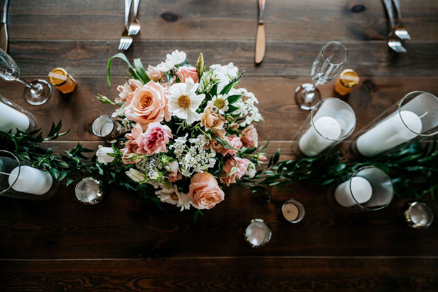 Elegant floral centerpiece with pink roses and candles on wooden table.
