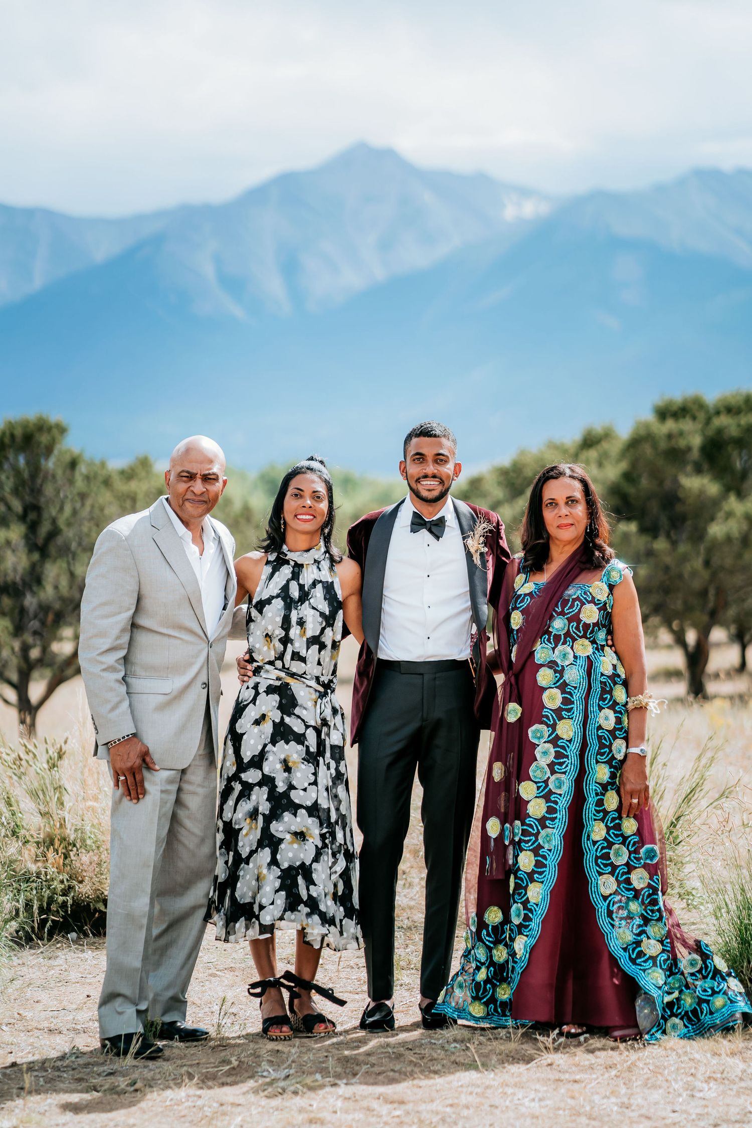 Small group dressed in formal attire posing together with mountains in the background.