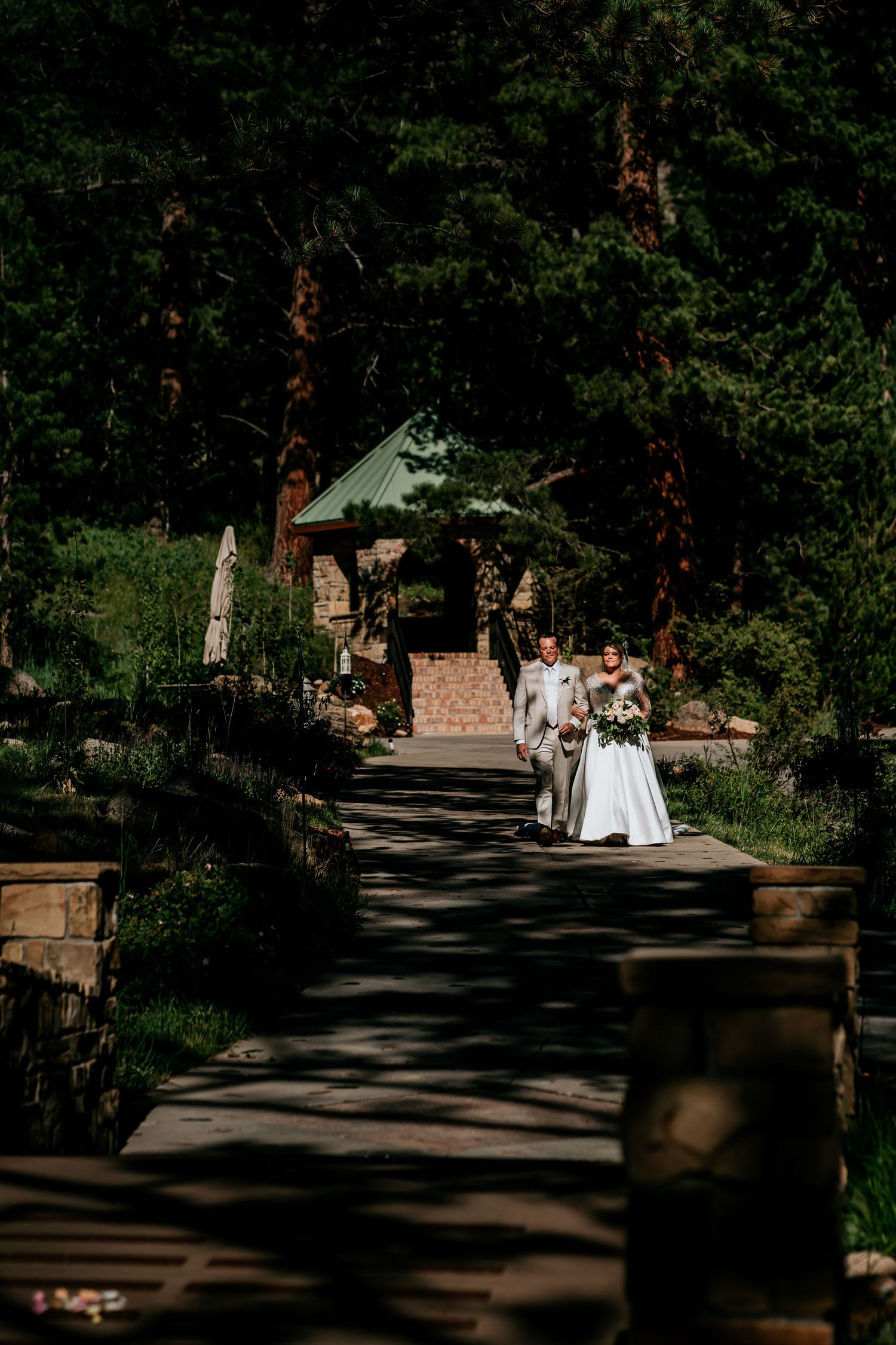 Stone pathway leading to a quaint chapel surrounded by tall pine trees.
