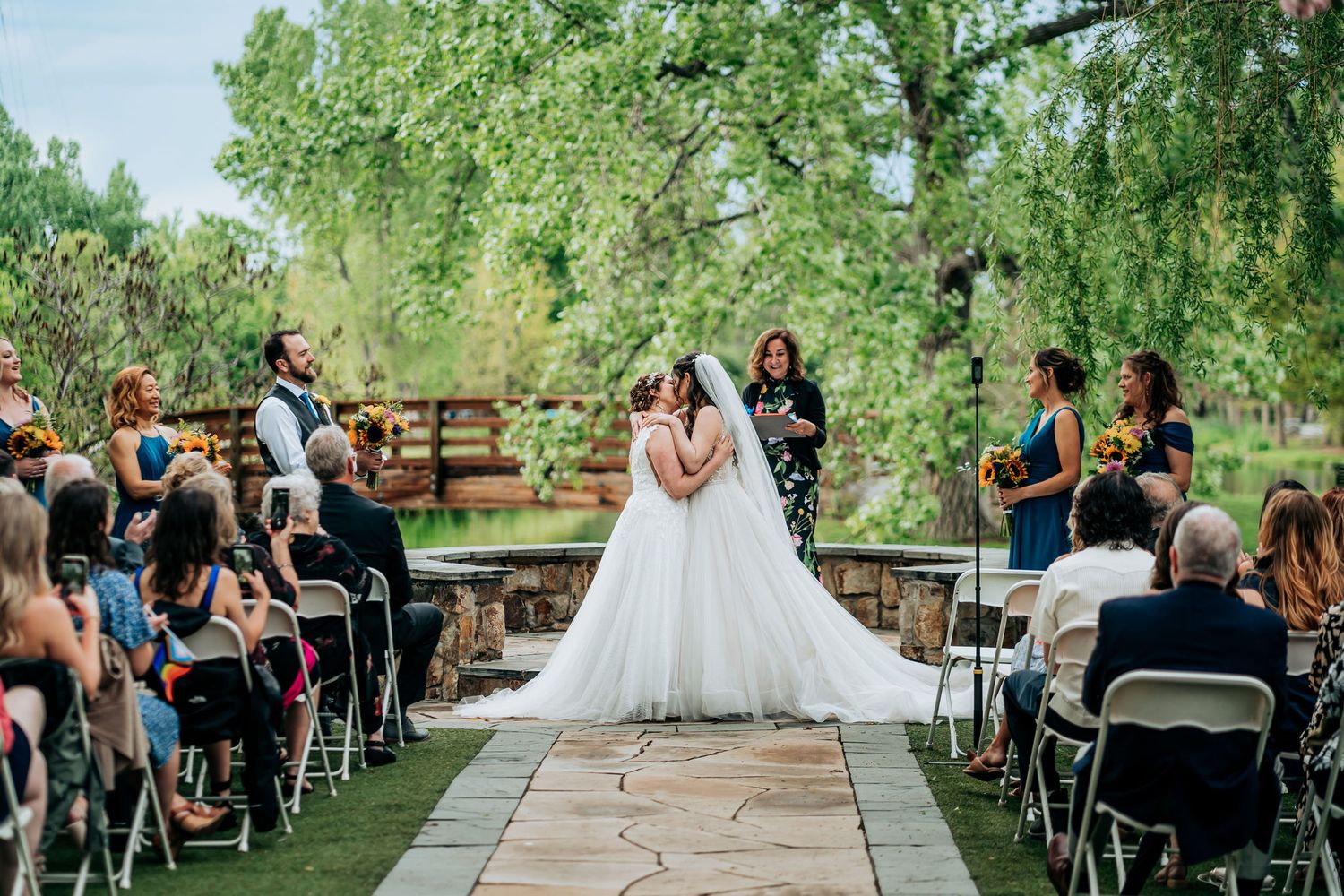 Wedding ceremony on stone patio with guests seated under green trees.