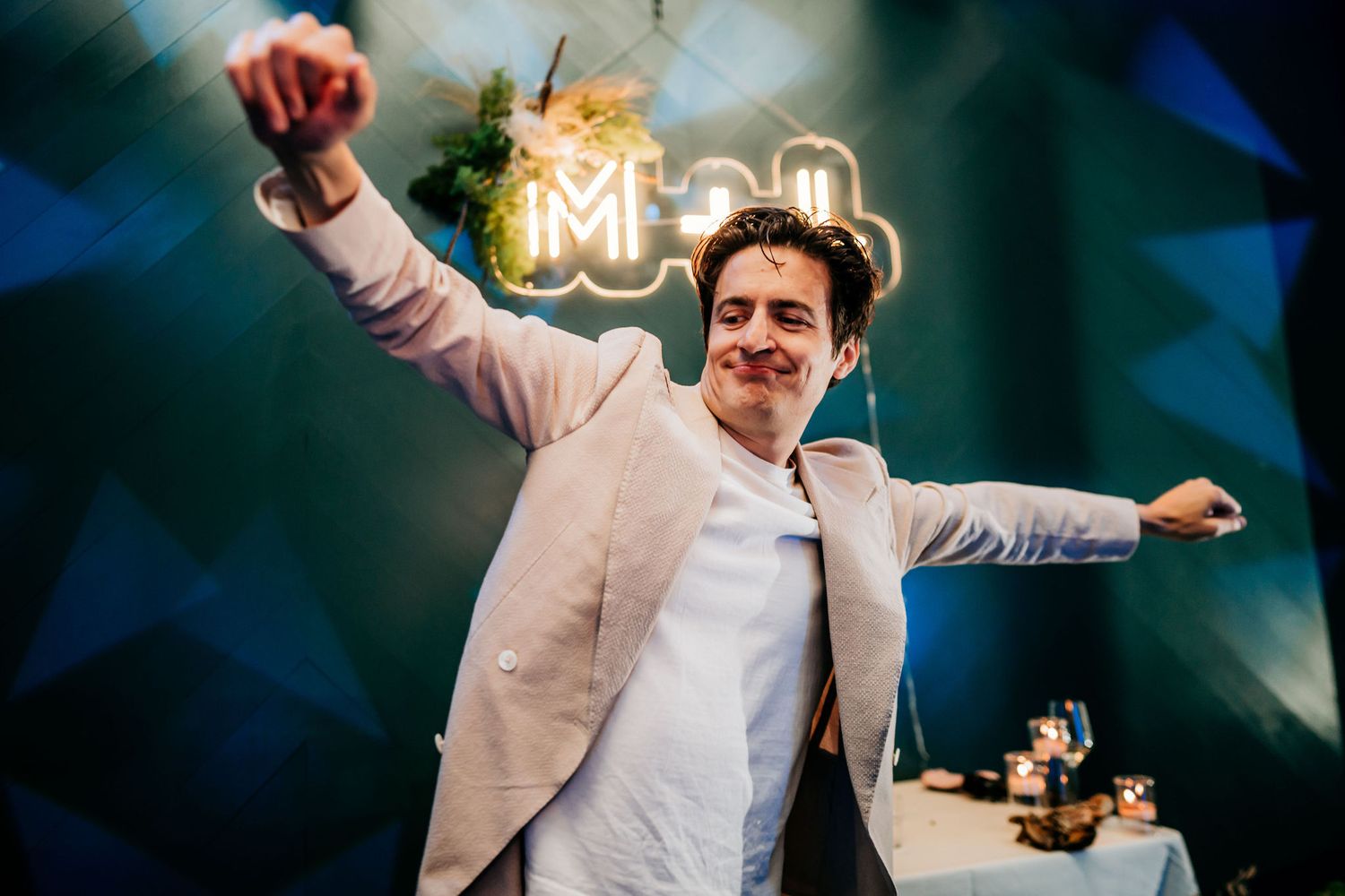 Person in pink blazer dances energetically against a blurred background with illuminated signage.