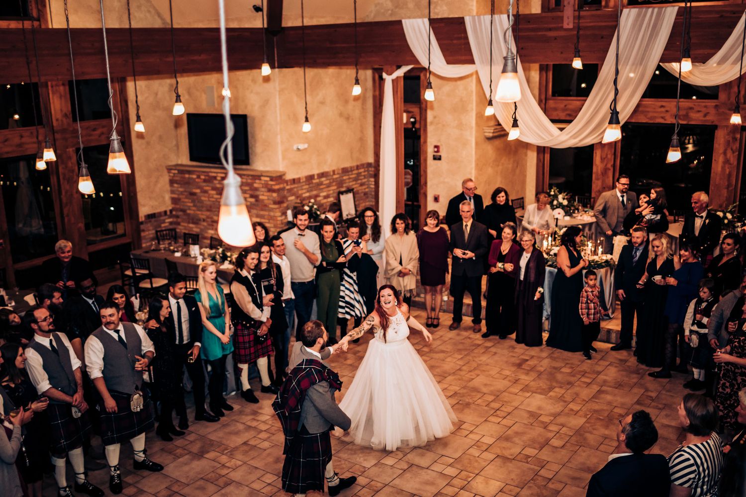 Wedding reception dance in rustic venue with white draping and string lights.