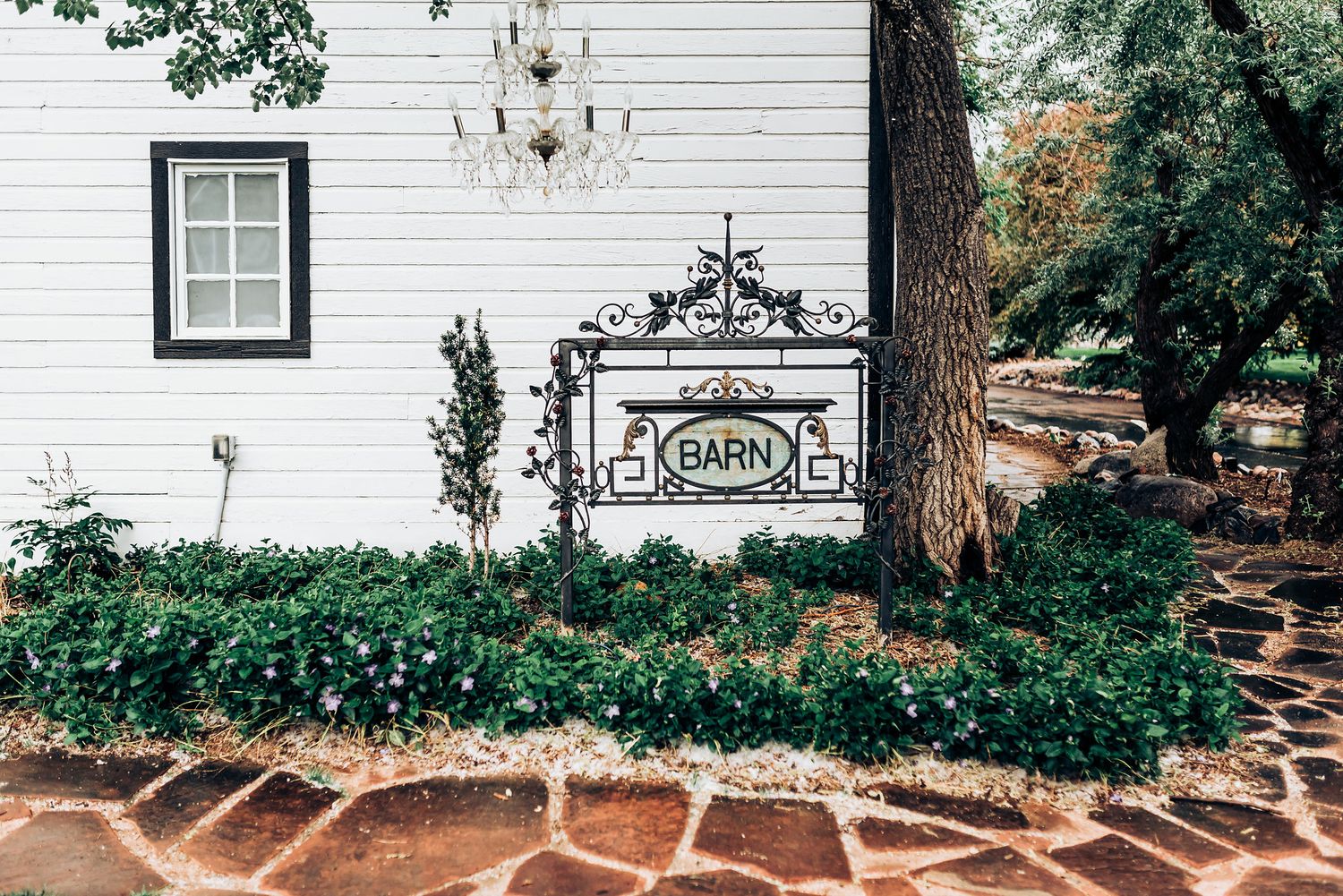 White garden sign mounted on classic white siding with landscaped stone pathway.
