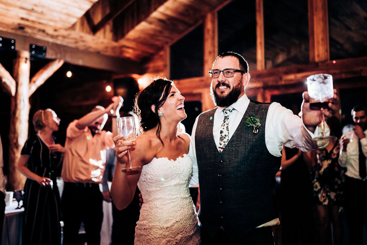 Couple celebrates on dance floor while guests cheer at rustic wedding reception.
