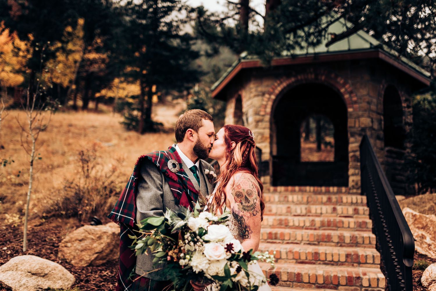 A couple shares an intimate moment by a stone archway with a bouquet of white flowers.