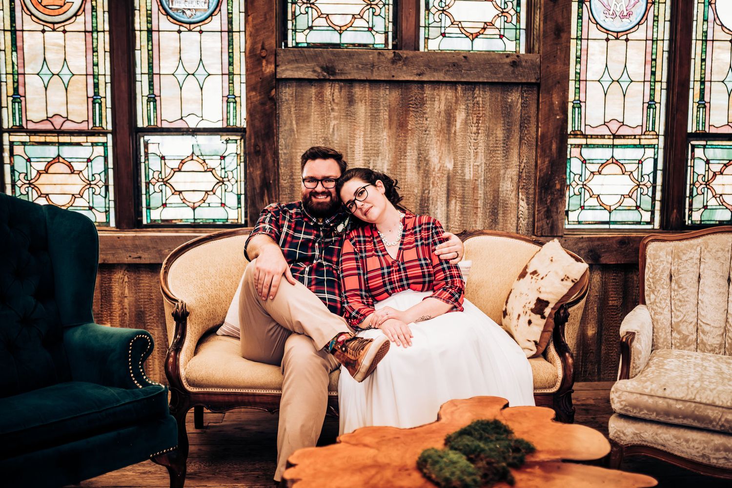 Intimate wedding portrait on vintage sofa with stained glass windows and floral decor.