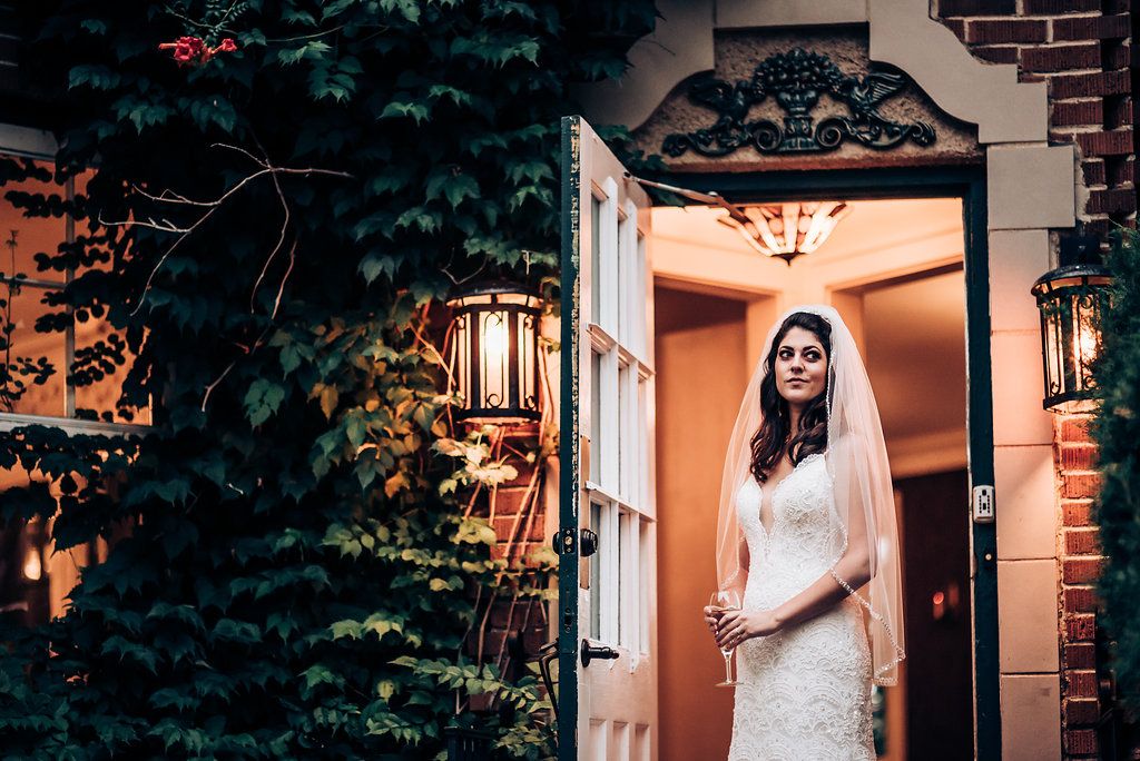 A bride in a lace gown poses elegantly in an ornate doorway with lanterns.