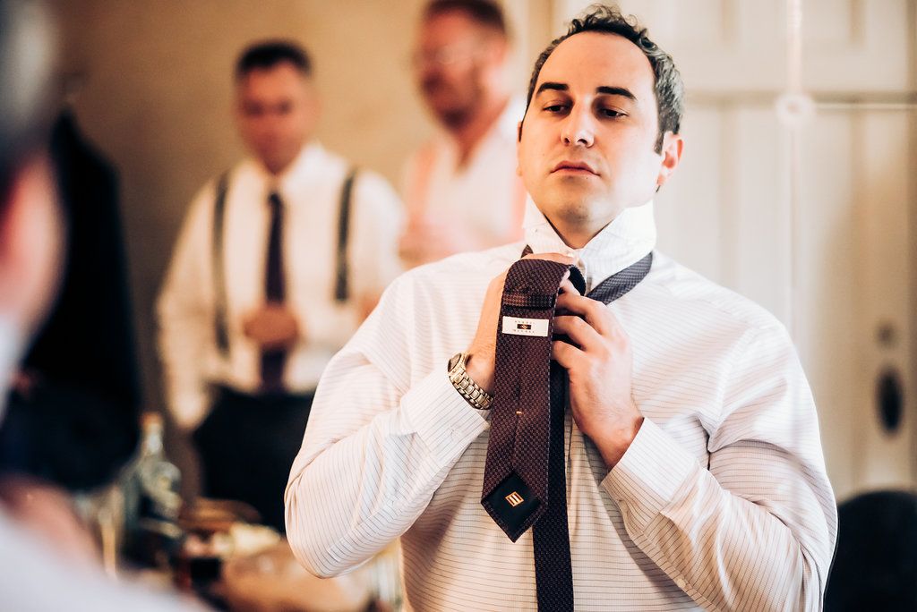 A man in formal attire adjusts his dark tie while getting ready.