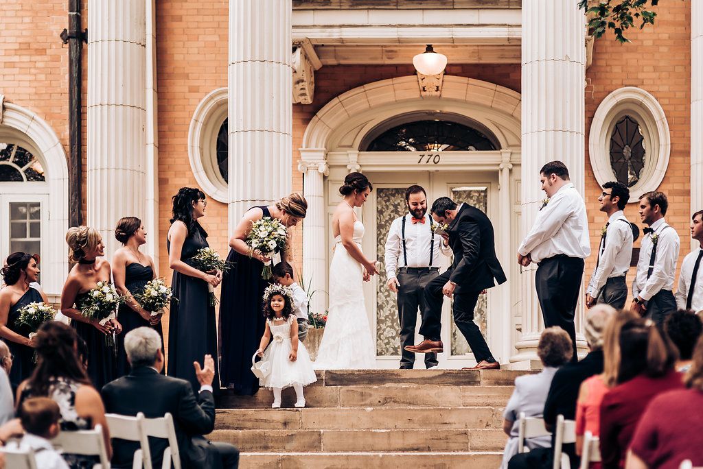 Wedding ceremony on historic building steps with guests seated on white chairs.