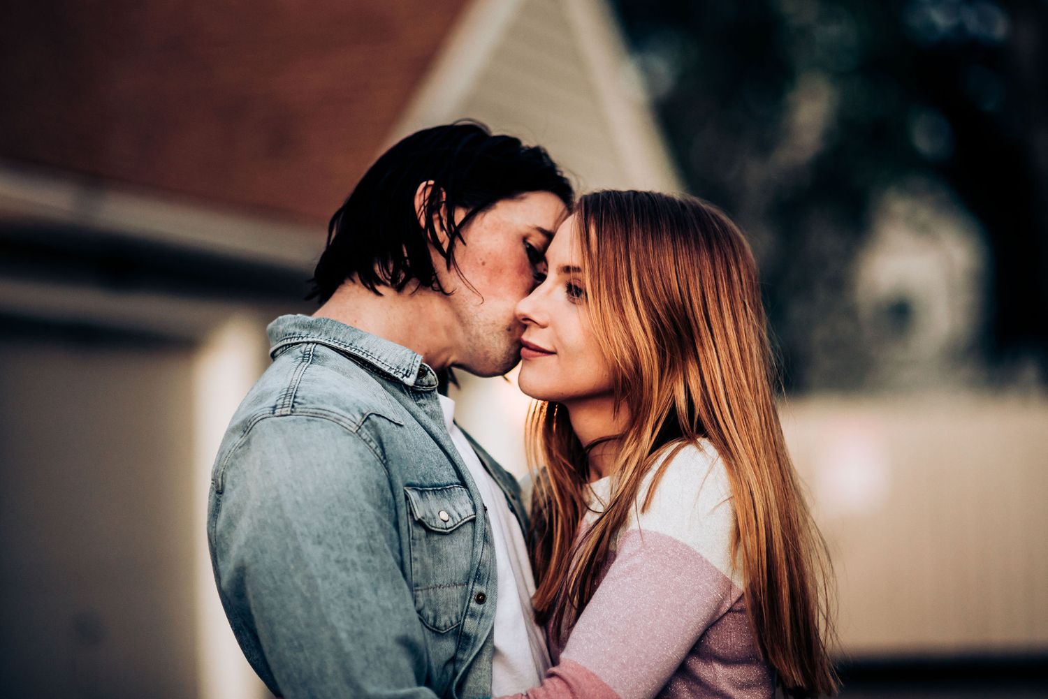 A tender romantic moment between a couple in casual attire against a blurred background.
