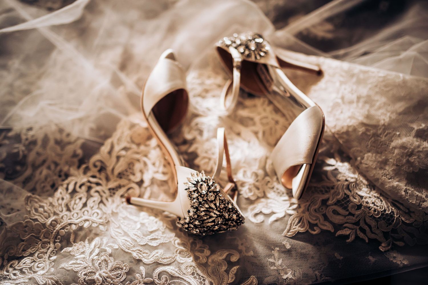 Ornate wedding heels with jeweled details resting on delicate lace veil.