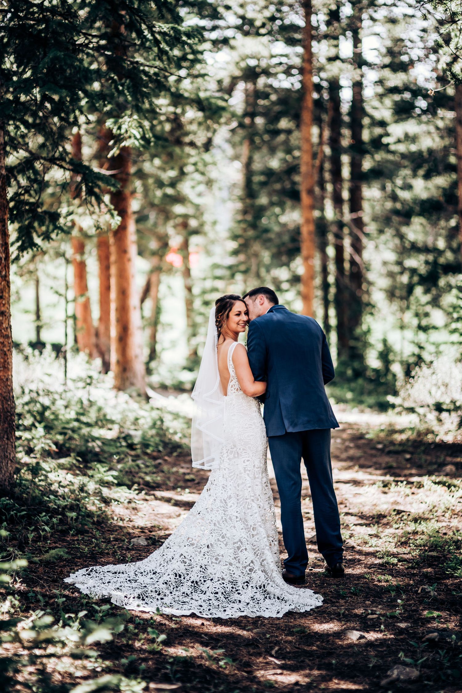 The intricate lace detail of a wedding dress catches sunlight on a forest trail.