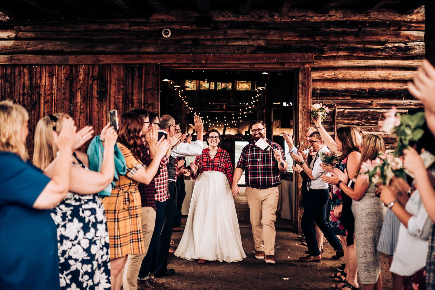Wedding celebration in rustic barn venue with crowd of guests cheering.