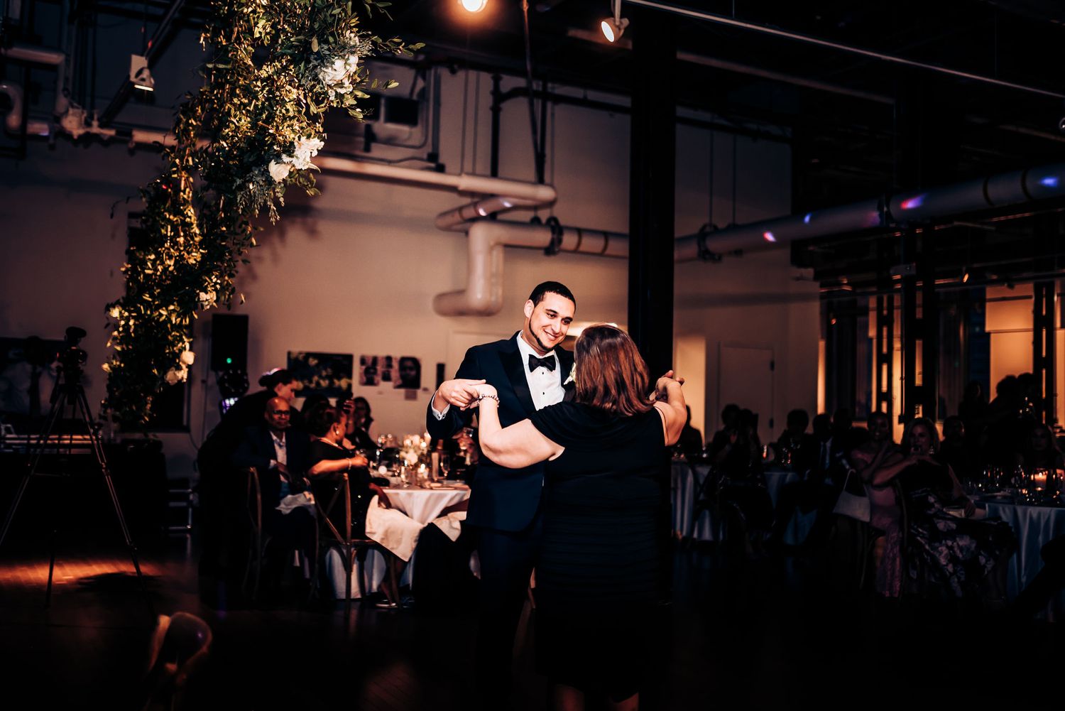 A couple shares a romantic first dance at their wedding reception under decorative floral arrangements and ambient lighting.