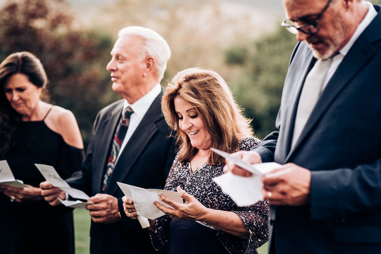 Several people in formal attire reading papers together during an outdoor gathering.