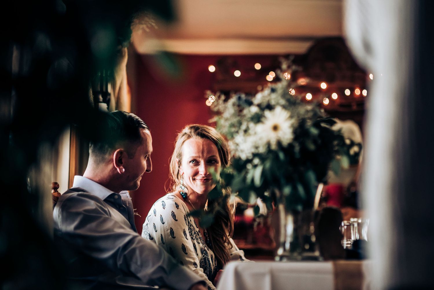 Candid moment captured at wedding reception with soft lighting and floral centerpieces in background.