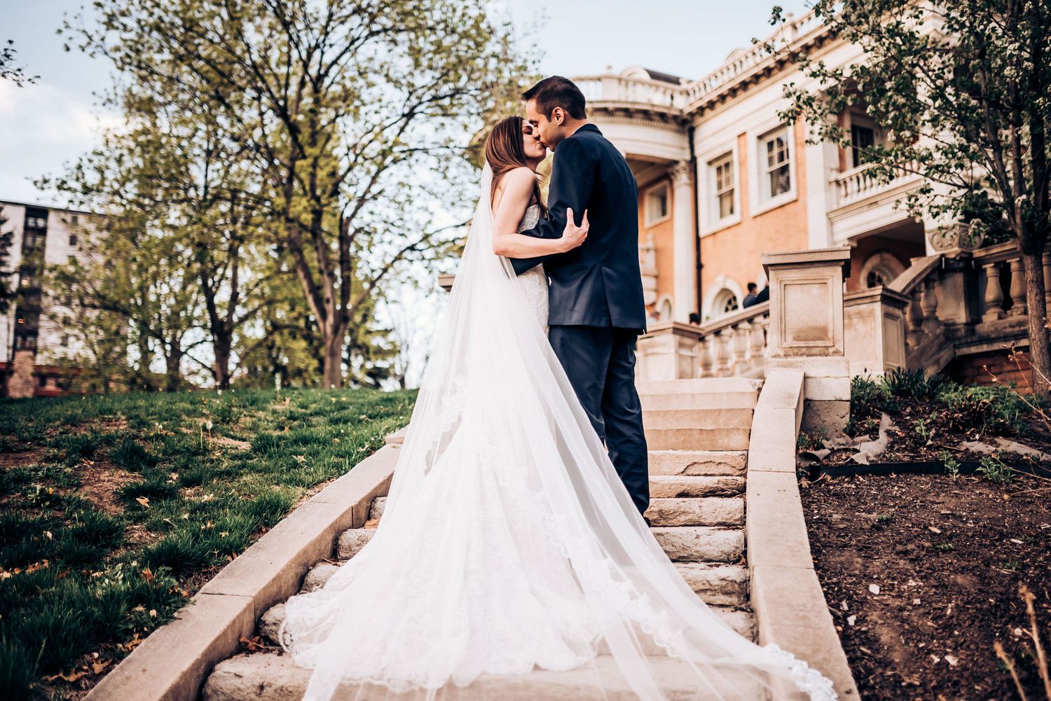 Romantic wedding portrait on stone steps with bride's dress flowing dramatically.