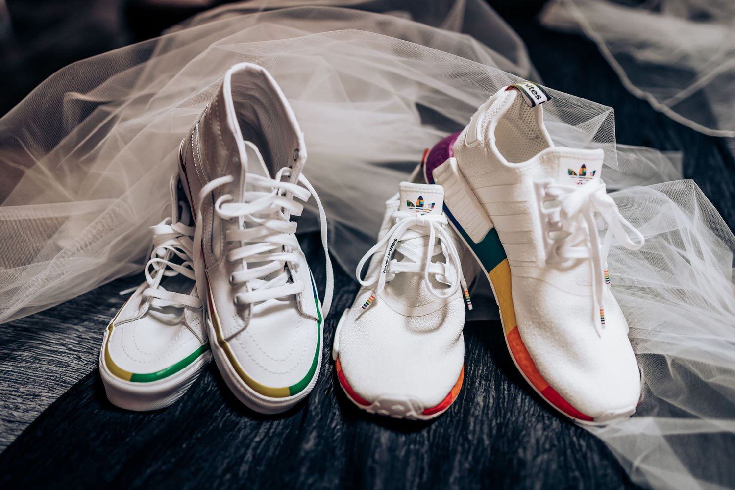 White wedding sneakers arranged with delicate veil on dark surface.